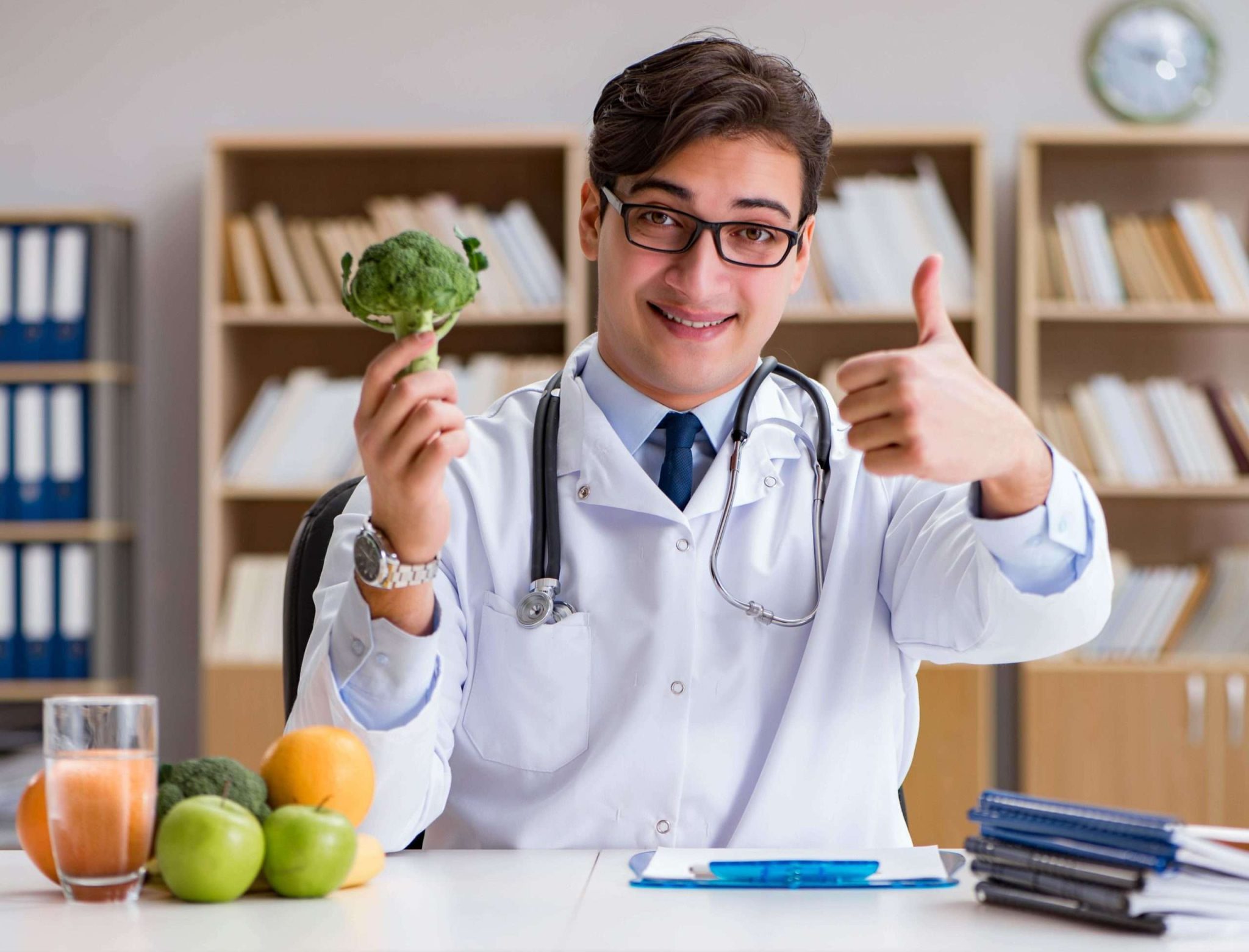 A doctor is giving thumbs up gesture with broccoli in his hands.